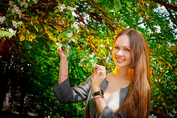 Outdoor portrait of a beautiful young girl near blossom apple trees with white flowers.