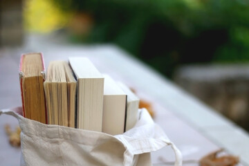 Canvas tote bag filled with books in the garden. Selective focus.