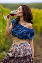 A beautiful woman with a glass of red wine in the vineyard on autumn day.