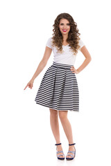 Beautiufl Young Woman In Striped Skirt Is Standing And Pointing Down.