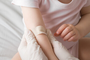 Doctor in white rubber protective gloves putting adhesive bandage on baby arm vein after blood test...