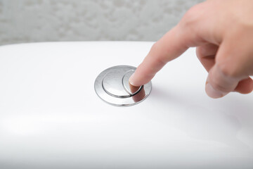 Young woman hand finger pushing button in toilet. Closeup.