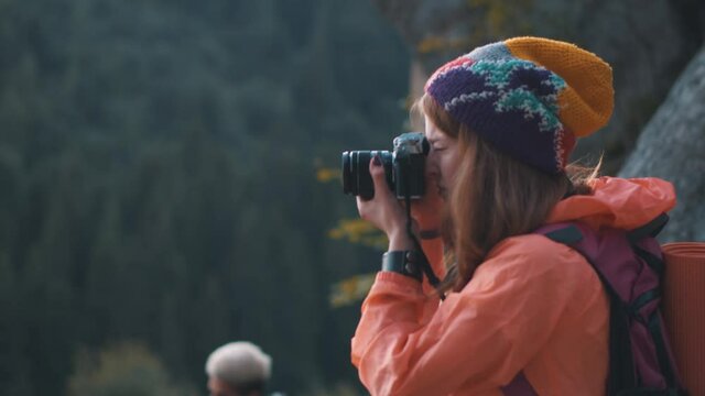 Cheerful caucasian redheaded girl tourist standing in the mountains taking stunning pictures landscape scenery outdoor. Group of friends travel to the woods. Leisure activity.