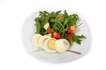 Fresh vegetable salad with egg, tomatoes, cucumbers and arugula on a plate isolated on a white background