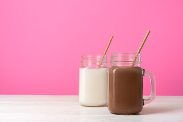Glass jars with flavoured milkshakes against pink background