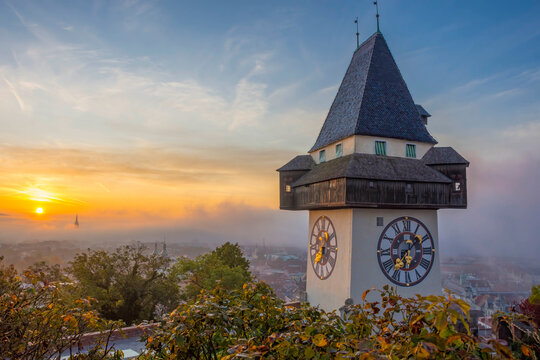 The famous clock tower on Schlossberg hill, in Graz, Styria region, Austria, at sunrise. Beautiful foggy morning over the city of Graz, in autumn