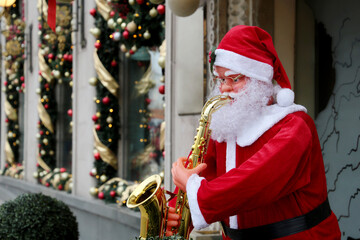 Statue of Santa playing the trumpet on a city street. Shop window decorated with Christmas ornaments