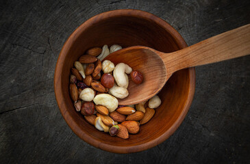 Nuts on a wooden background in a plate. Various types of nuts such as hazelnuts, almonds, walnuts and pistachios are scattered on a wooden background. View from above