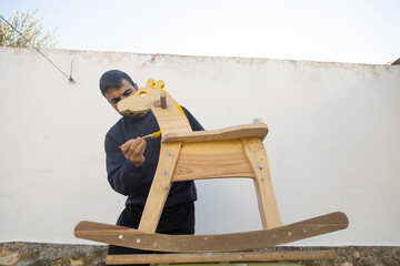 man painting homemade giraffe-shaped rocking horse