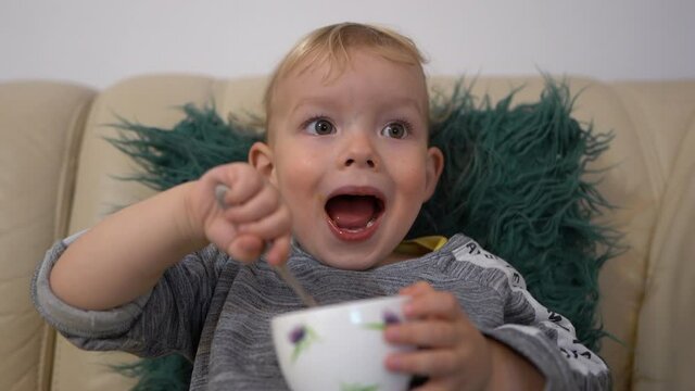 Boy watching cartoons and eating mango ice cream. Close indoor portrait of a blond three-year-old. Happy childhood, leisure child concept