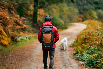 A hiker in a red coat and brown backpack walking with his dog on a mountain path in spring or fall. Mountain and trekking. Adventure, Art, Travel