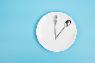 Top view white ceramic plate with knife, spoon and fork on blue background. Intermittent fasting, Ketogenic dieting, weight loss, meal plan and healthy food concept
