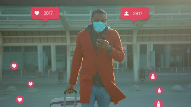 Serious young African man in stylish clothes with suitcase leaving airport after landing. Guy in face mask with phone in hands picking up wifi, internet popularity. Ways to prevent coronavirus