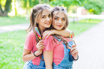 two beautiful twin girls hugging in denim overalls with lollipops