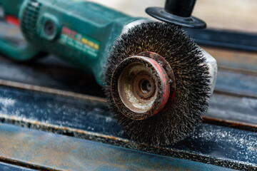 Worker cleans rust on steel using an electric wheel grinding machine.