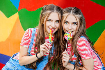 teenage twin sisters in colorful clothes with lollipops on colorful graffiti background