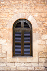 Fototapeta na wymiar Arched window with closed shutters on stone wall