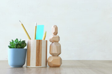 Stylish and minimal workplace with plant, pencils stand and dummy over wooden desk work