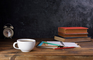 White coffee cup with dark black coffee And old books And the clock is arranged on an old wooden table and a black wooden wall.