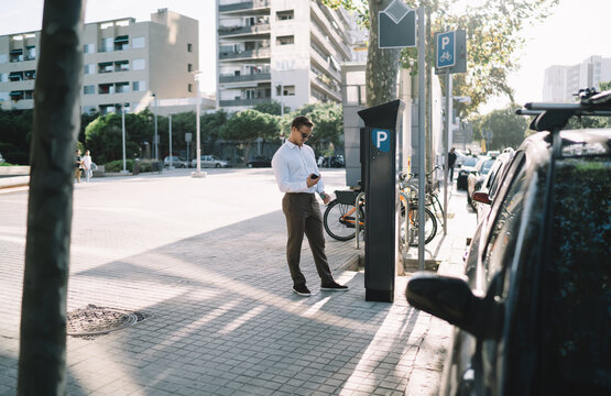 Caucasian businessman ticketing in parking meter during time in financial district of megalopolis, formally dressed male manager checking security payment via credit card at terminal machine