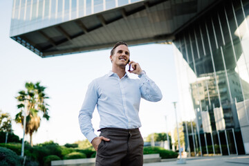 Smiling male director holding hand in pocket while answering phone call in downtown