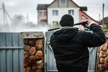 Cleaning dirty stone fence using high pressure power washer.