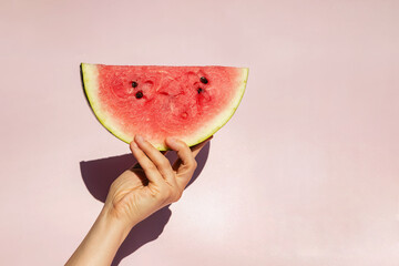 Feminine hand holding slice of ripe watermelon over pink backgroun