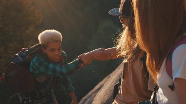 Help me, please. Smiled tourist helping to his friend hiking a mountain with handshake. Friendship support trust concept. Forest, cliffs background. Active tourists hiking at summer fall day in nature