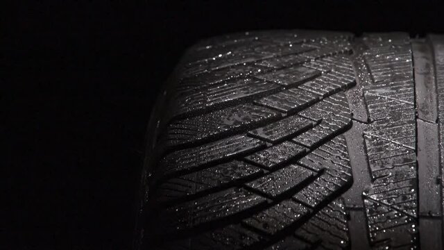 Tire Tread in Water Droplets. Loop. The geometric pattern of the wheel in water droplets slowly rotates towards the viewer. Drops sparkle on the black rubber on a black background