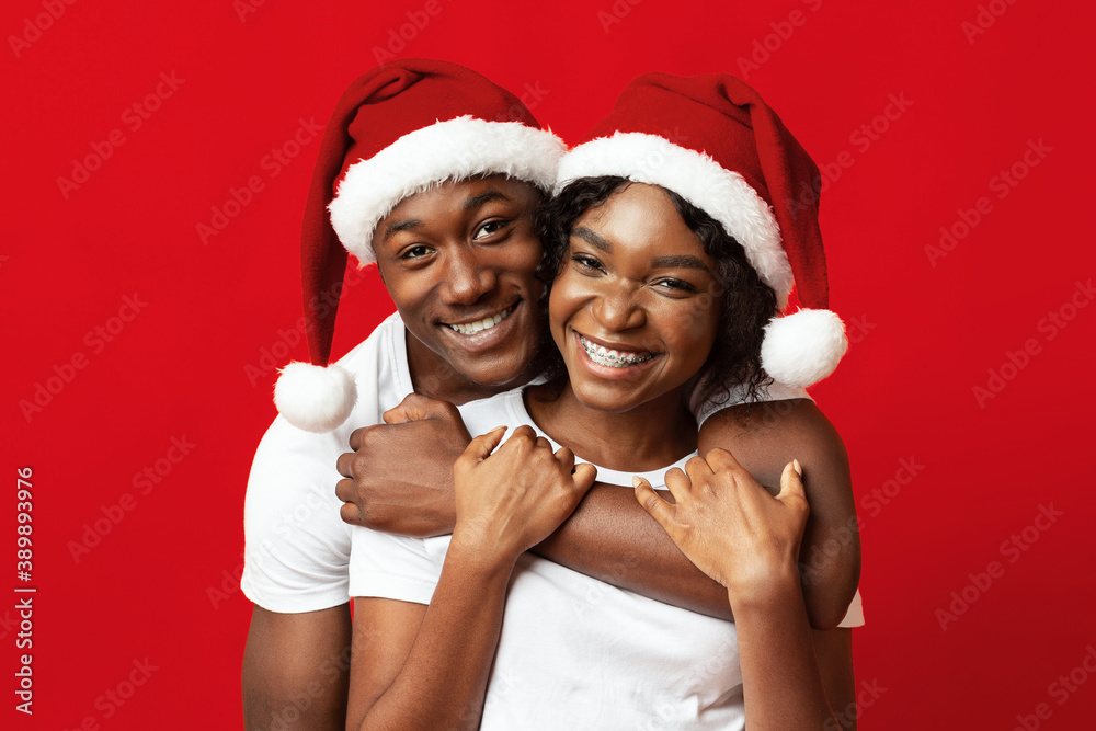 Wall mural young black lovers in santa hats having fun on red