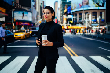 Stylish businesswoman with smartphone and coffee on street