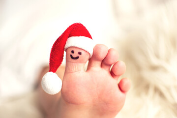 Child big toe with santa hat and smiling face.  Closeup photo of caucasian foot. Christmas and barefoot concept with copy space.