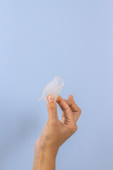 Woman hands holding menstrual cup on pastel blue background. Zero waste alternatives, hygiene period product. Copy spase