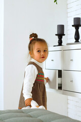 a little girl in a white jacket and a brown dress with a bun on her head in a white room