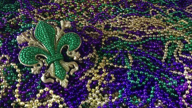 Sparkling fleur de lis in green on pile of colorful Mardi Gras beads
