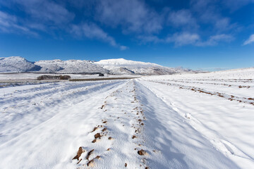 Wide agle view of a ploughed farmland on a hill covered in thick snow with matroosberg Mountain on...