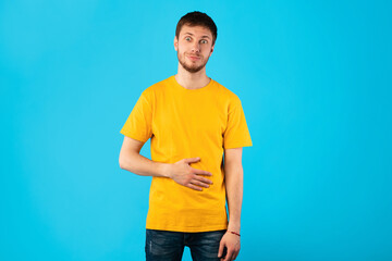 Young satisfied man touching his stomach at studio