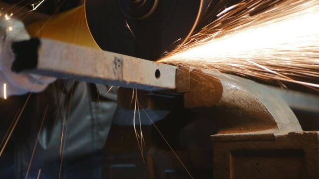 A locksmith worker cuts off a piece of steel pipe with a circular saw. Sparks from the grinder light up the darkness. work with cutting and grinding steel. 4k