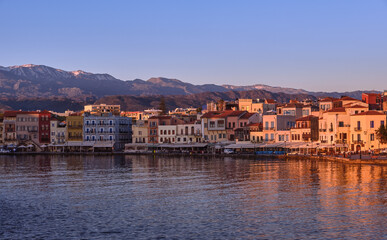 Fototapeta na wymiar Sunrise at Old Venetian harbour of Chania, Crete, Greece, shop, hotels, cafes and restaurants on its quay in first sunrays. Cretan hills and mountains