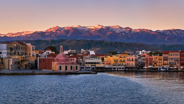 Sunrise view of Old Venetian harbour of Chania, Crete, Greece, its quay side. Great Cretan mountains covered with snow. Former mosque Giali Tzamisi