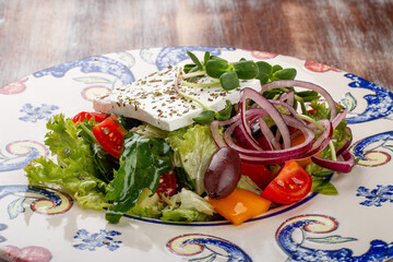 Greek salad on a decorative plate. On a wooden background