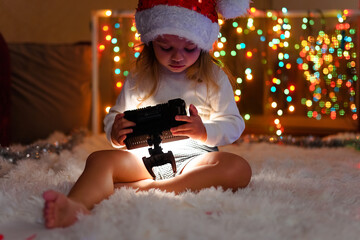 a little girl in a Santa hat sits near the Christmas lights with a lantern