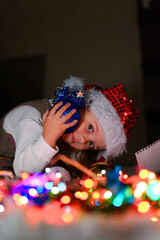 a little girl in a Santa hat sits near the Christmas lights
