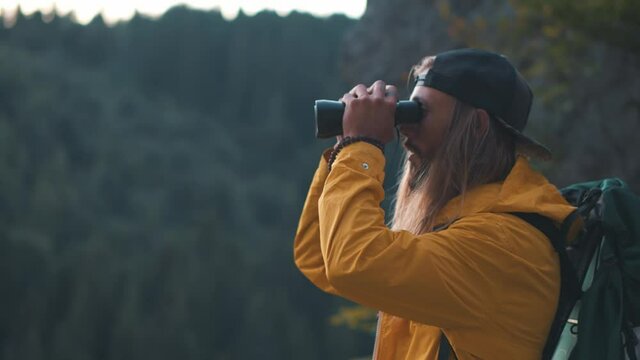 Caucasian hipster man using binoculars birdwatching or looking at natural scenery searching ways traveling with group of friends. Nature concept. Forest environment. Camping.