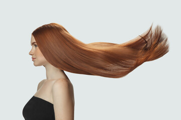 Silk. Beautiful model with long smooth, flying red hair isolated on white studio background. Young girl with well-kept skin and hair blowing on air. Concept of salon care, beauty, fashion.