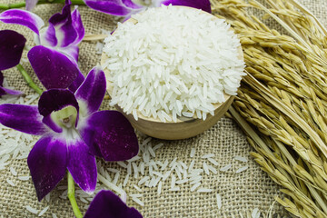 The rice is in a wooden cup and paddy rice and an orchid are placed on the hemp sack.