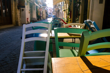 Early morning, empty narrow streets of old mediterranean town. Bright sun. Colorful chairs and tables in cafes. Selective focus. Chania, Crete, Greece
