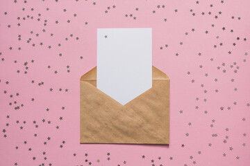 Kraft paper envelope letter with blank white card mockup on pink background with confetti stars. Christmas, New Year, Birthday concept. Holiday mockup.Top view with place for text.