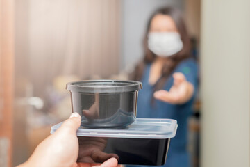Food delivery during corona virus outbreak. Asian woman wearing face mask receiving healthy food delivery boxes, Lunch box from delivery man at the door. Focus on food box
