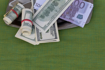On a green background on a metal tray are banknotes of dollars and euros..